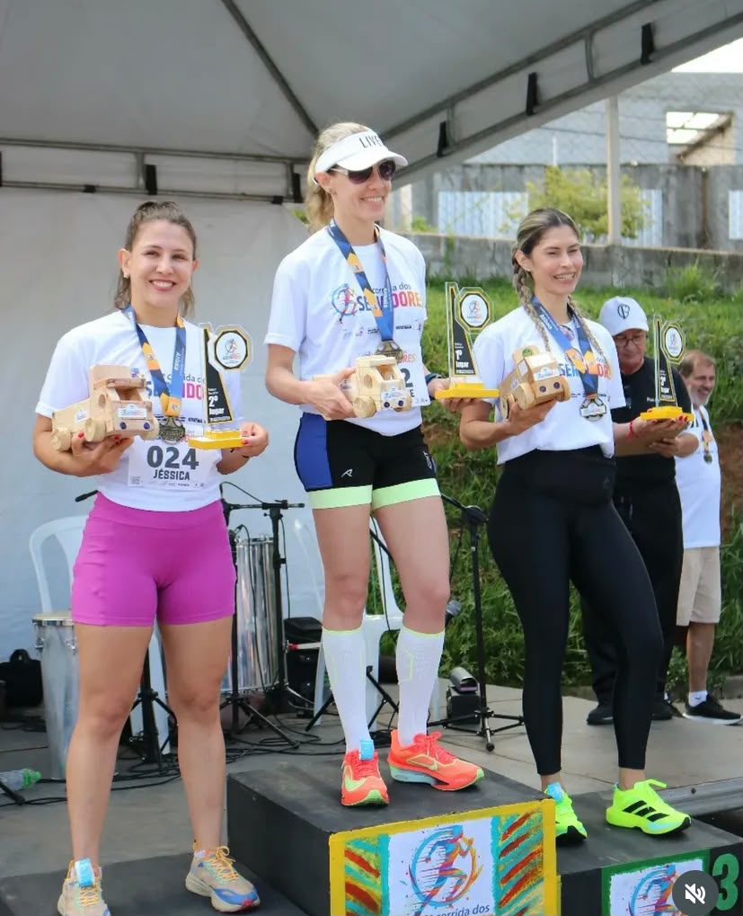Vencedoras exibindo troféus de madeira no pódio